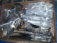 Top view of a box containing assorted silver plated flatware and serveware pieces including cake servers, ornate forks, and ladles.