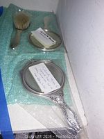Three items on shelf: ornate mirror, round mirror, hair brush