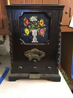 Front view of wooden cased Thomas Collectors Edition radio with floral embroidery on front cover, control knobs, and metal badge