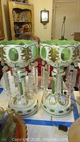 Overall view of both white milk glass mantel lamps with green ovals and hanging crystal prisms, displayed side by side.