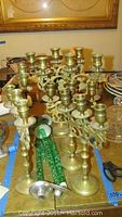 Photo showing all six brass Shabbat candelabras arranged on a table among other items, clearly showing the four smaller and two larger candelabras.