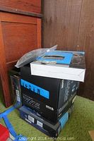 Stacked boxes containing Sirius Starmate and other Sirius satellite radio kits and accessories placed on floor near wooden furniture.