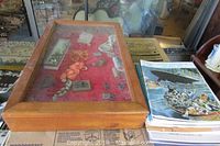 Overview of wooden display case with various costume jewelry and a stack of Titanic Commutator magazines beside it