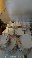Stack of plates, cups, saucers and bowls showing floral pattern and gold trim