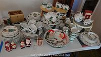 Wide shot showing three sets of Christmas-themed dinnerware on a table, plus holiday figurines in front.