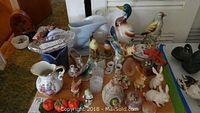 Overview showing assorted pressed glass dishes, ceramic and porcelain pitchers, rabbit, bird, and egg figurines displayed on a surface.