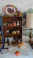 Full view of shelf with Thanksgiving and collectible themed items including turkey plate, bisque figurines, bird plates, mugs, cut glass, pumpkins.