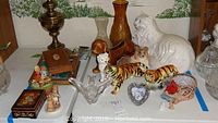 Wide view of Hummel themed items and ceramic animals arranged on a table including large white cat, ceramic tigers, small dogs, and small decorative pieces.