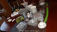 Various pieces of clear pressed glass, green glass items on marble bases, and white china on a table.
