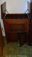 Vintage wooden bar stand with top open and bottom doors open, showing compartments and bottle holders