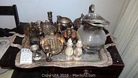 Full lot of silver plate items on serving tray including pitcher, creamer, sugar bowl, candelabra holders, salt and pepper shakers, tongs, all showing tarnish and wear.
