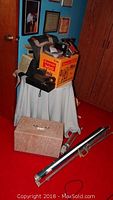 Lot overview showing Brownie 300 movie projector in box, other cameras stacked on table, tripod on floor.