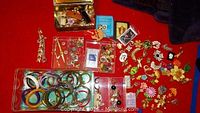 First photo showing an assortment of bracelets, bangles, brooches, pins, and watches laid out on red fabric.