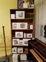 Bookshelf filled with ten original boxes of Department 56 Heritage Village buildings. Boxes show black and white sketches of the buildings on the front, stacked on five shelves.
