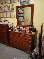 Photo showing the cherry finish four drawer dresser with metal handles and various items on top, next to matching mirror.