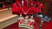 Full side view of large red glass ruffled bowl on decorative metal base with crystal pendants
