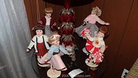 Photo showing all six ceramic dolls arranged on a glass table with a red decorative lamp in the background. Dolls include a cheerleader, a boy in a letterman jacket, and other female dolls.