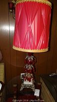 Full view of one lamp showing the red pleated fabric shade, metal base with white marble top, and red glass crystal body with metal accents.