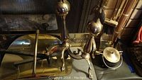 Photo showing brass fireplace tools including eagle-topped andirons, tool stand, wood basket, cast iron pot with brass lid, and fire starter rod.