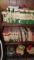 Shelf of green and white AMPEX reel to reel tape boxes with red stickers showing titles and numbers.