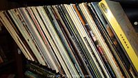 Photo showing a large stack of vinyl records in their sleeves packed vertically on a shelf.