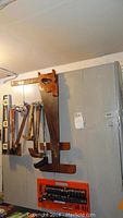 Wall mounted cabinet with handsaws, hammers, and other hanging tools.