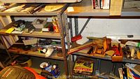 First image showing two metal shelving units with tools, painting supplies, and boxes including a staple gun kit.