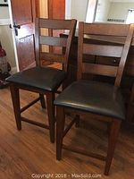 Two matching wooden ladder-back bar stools in front of wooden sideboard