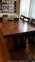 Solid wood dining table displaying natural wood grain and shades of warm brown, with four matching wooden chairs, visible nicks and scrapes on the tabletop surface.