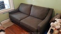 Full view of deep grey sleeper sofa with two seat and back cushions, placed near a window on wooden floor.