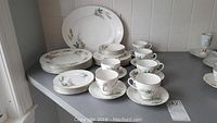 Full set of Mayfair bone china dinnerware arranged on countertop showing plates, teacups, saucers and serving platter.