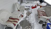 White wicker outdoor furniture set on snowy porch including loveseat sofa with striped cushion, 2 armchairs with striped cushions, and a round wooden top side table. Snow visible on and around furniture.