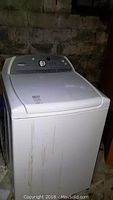 Front and right side view of white Whirlpool Cabrio top load washing machine, showing height and wear marks.