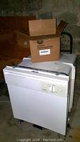 Photo shows Hotpoint dishwasher with box labeled as genuine replacement part on top, useful to convey included spare motor and dishwasher condition.
