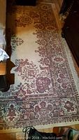 Traditional floral patterned area rug with cream base and red and brown designs, showing general condition and wear pattern