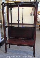 Front view of wooden curio/display cabinet, showing decorative top, mirror back on middle shelf, and panel with nailhead trim on bottom section.