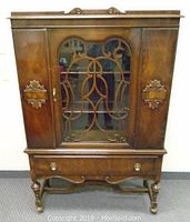 Front view of walnut china cabinet with central glass door containing fretwork, side wooden doors, drawer, and turned legs