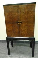 Closed floor model radio cabinet showing wood grain patterned doors and black stand with carved corners.