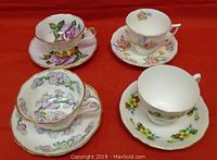 Four vintage English teacups and saucers arranged on red background showing floral designs and gold trim.