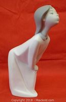 Side profile of Lladro Girl Kissing figurine showing bent posture and hands behind knees, matte white finish and gray hair.
