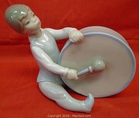 Front and side angled view of the boy holding a drum and a drumstick, showing facial features and clothing details.