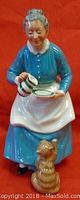 Frontal view of the Royal Doulton figurine showing the woman in blue pouring from striped jug with cat sitting in front.
