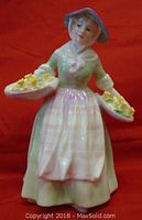 Front view of the Royal Doulton Daffy Down Dilly figurine showing details of bonnet, apron, and flower baskets