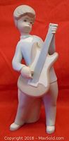 Front view of the white matte porcelain figurine of a boy playing guitar against red background.