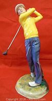 Full front view of Royal Doulton golfer figurine in yellow sweater and blue pants swinging a golf club against a red background.