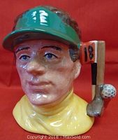 Front-facing close-up of the ceramic Toby Jug featuring the golfer's face, green visor, yellow neckerchief, golf club, and golf ball detail.