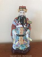 Front view of the signed 17 inch ceramic Asian male figurine on a wooden stand showing multi-colored robes and crown details.