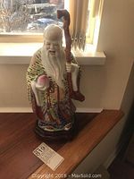 Full view of the ceramic Asian figurine on wooden stand with natural light showing overall design and colors.