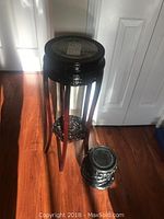 Tall black high gloss plant stand with four legs and carved lower shelf accompanied by one black carved vase stand on floor