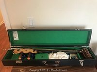 Open black hard-shell case with green velvet lining showing erhu instrument, bow, small boxes, and cloth.